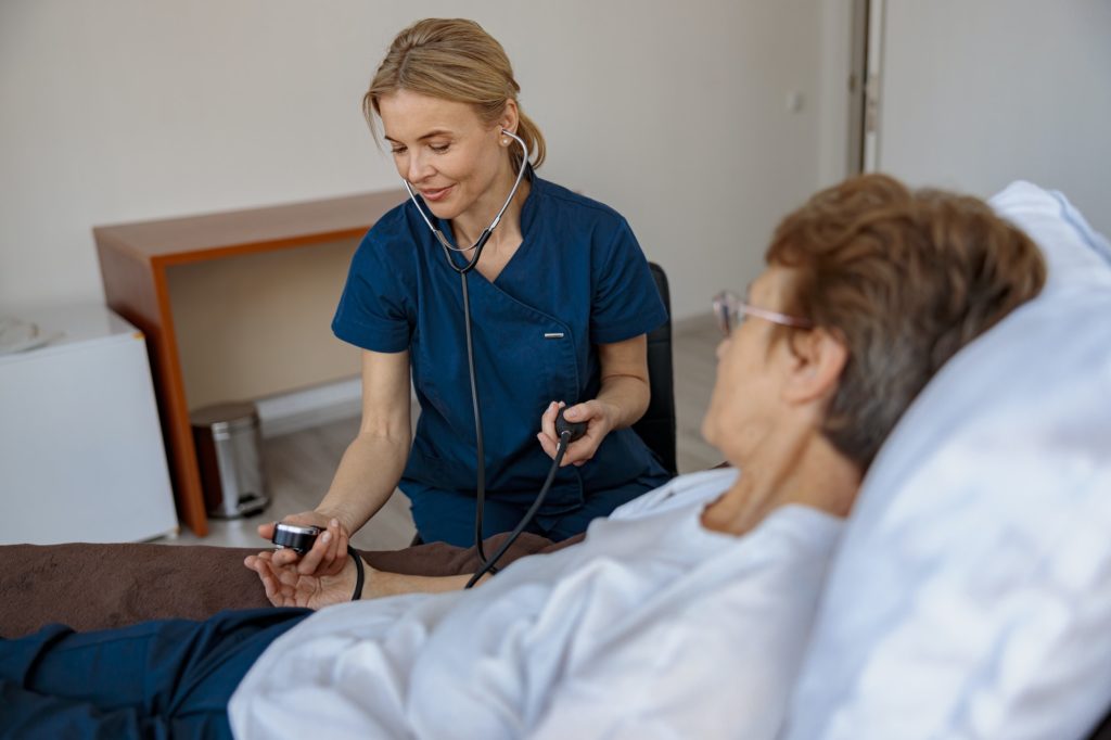 Female nurse checking blood pressure of senior woman in the ward of modern clinic